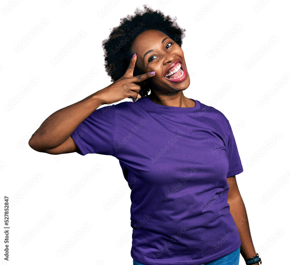 African american woman with afro hair wearing casual purple t shirt doing peace symbol with fingers over face, smiling cheerful showing victory African american woman with afro hair wearing casual purple t shirt doing peace symbol with fingers over face, smiling cheerful showing victory