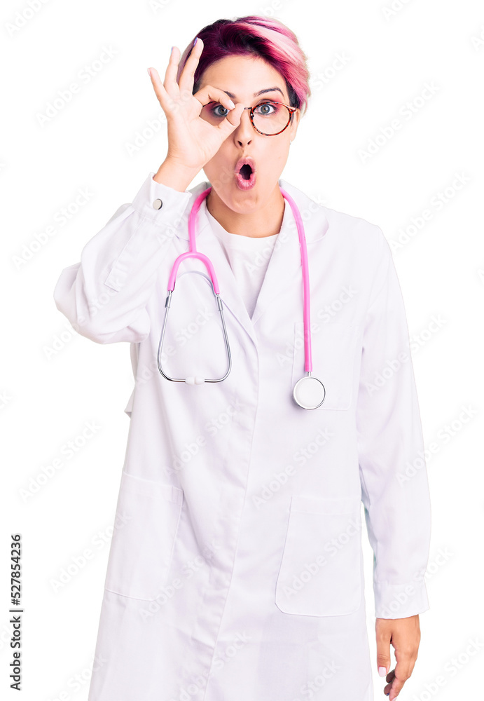 Young beautiful woman with pink hair wearing doctor uniform doing ok gesture shocked with surprised face, eye looking through fingers. unbelieving expression. Young beautiful woman with pink hair wearing doctor uniform doing ok gesture shocked with surprised face, eye looking through fingers. unbelieving expression.