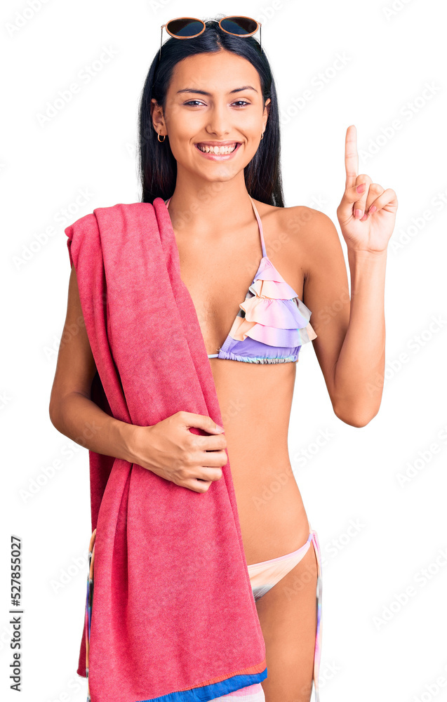 Young beautiful latin girl wearing bikini and sunglasses surprised with an idea or question pointing finger with happy face, number one Young beautiful latin girl wearing bikini and sunglasses surprised with an idea or question pointing finger with happy face, number one