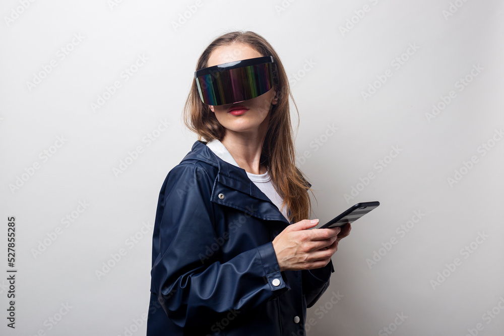 Young woman in virtual reality glasses with a phone in a blue jacket on a light background Young woman in virtual reality glasses with a phone in a blue jacket on a light background