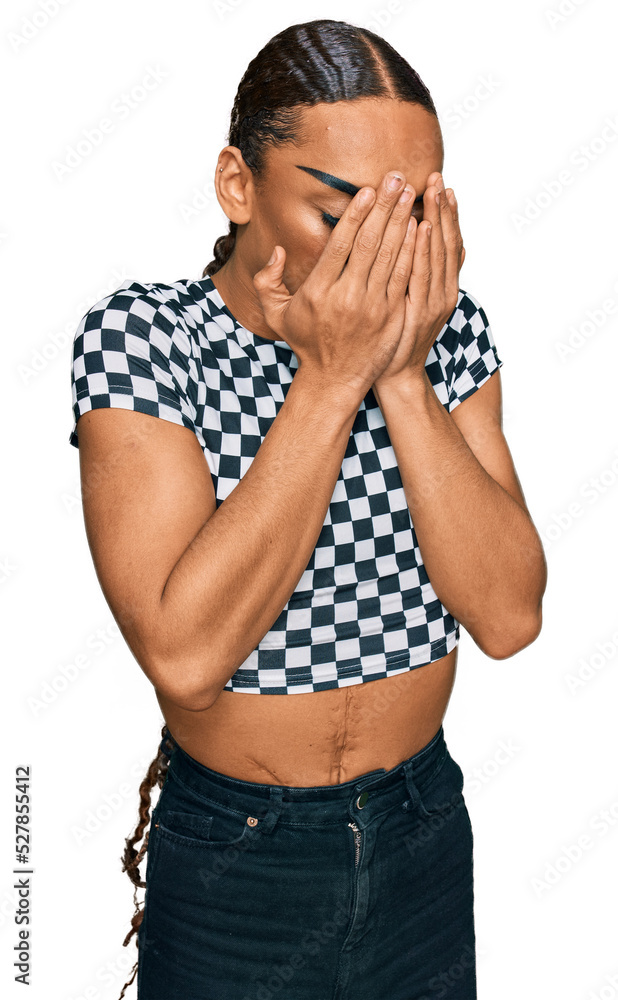Hispanic transgender man wearing make up and long hair wearing modern clothes with sad expression covering face with hands while crying. depression concept. Hispanic transgender man wearing make up and long hair wearing modern clothes with sad expression covering face with hands while crying. depression concept.