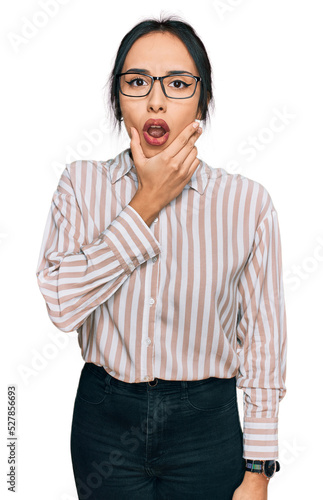 Young hispanic girl wearing casual clothes and glasses looking fascinated with disbelief, surprise and amazed expression with hands on chin