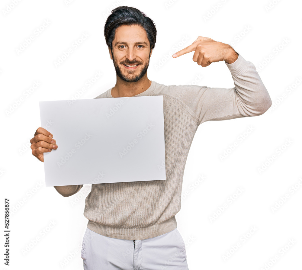 Young hispanic man holding blank empty banner pointing finger to one self smiling happy and proud Young hispanic man holding blank empty banner pointing finger to one self smiling happy and proud