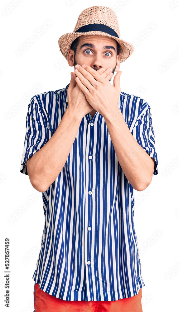 Young handsome man with beard wearing summer hat and striped shirt shocked covering mouth with hands for mistake. secret concept. Young handsome man with beard wearing summer hat and striped shirt shocked covering mouth with hands for mistake. secret concept.