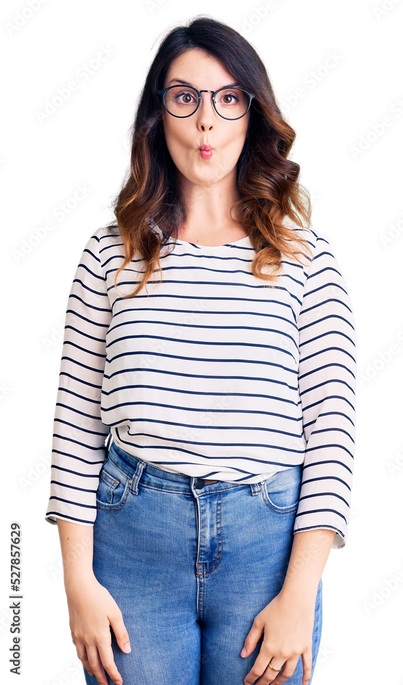 Fototapeta premium Beautiful young brunette woman wearing casual clothes and glasses making fish face with lips, crazy and comical gesture. funny expression.