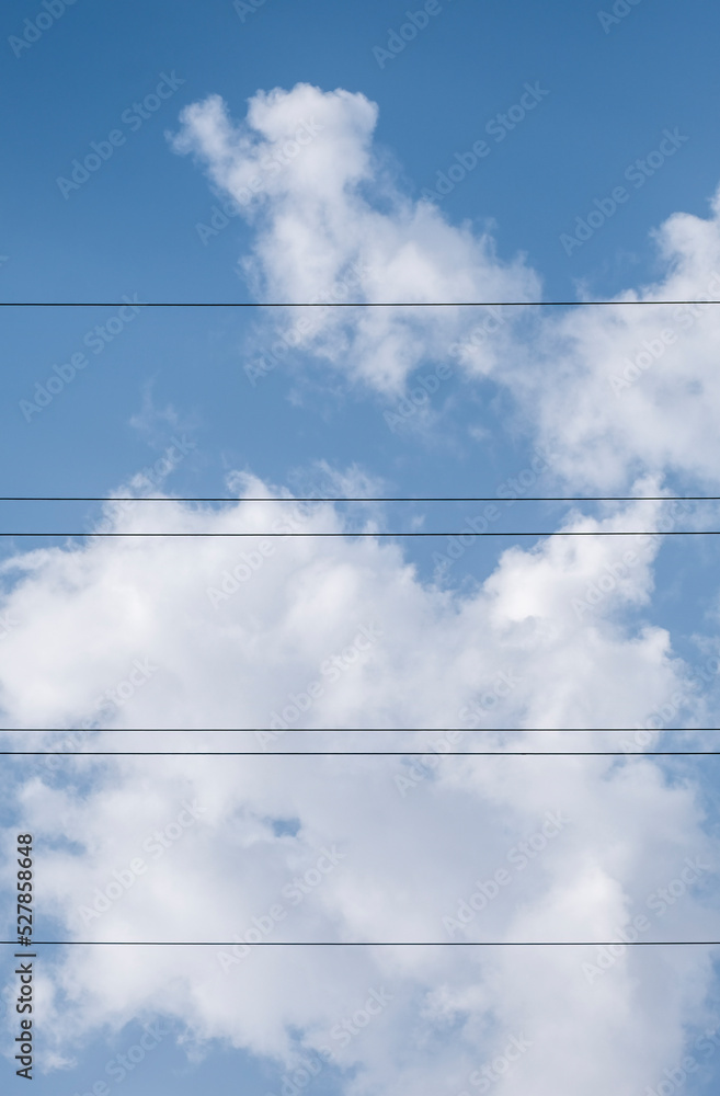 Cables of an electrical power line compose a score on a natural summy blue sky background with beautiful puffy white cumulus clouds Cables of an electrical power line compose a score on a natural summy blue sky background with beautiful puffy white cumulus clouds