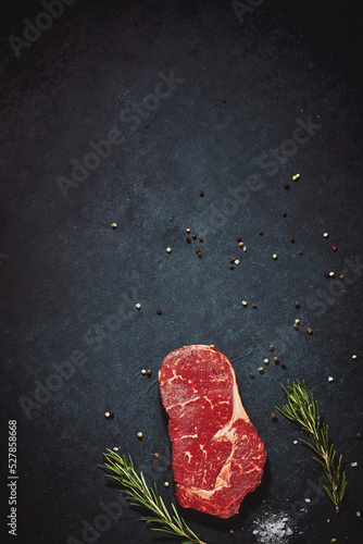 Dark textured kitchen countertop with slice of red meat, rough salt crystals and spices