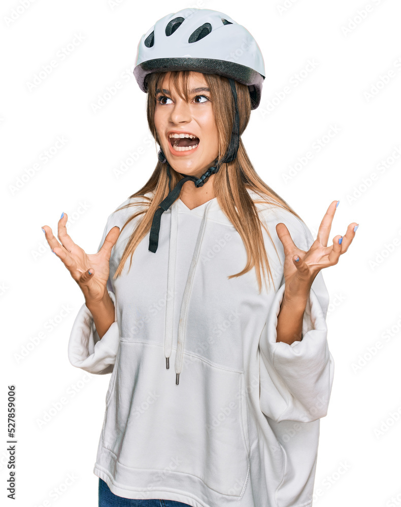 Teenager caucasian girl wearing bike helmet crazy and mad shouting and yelling with aggressive expression and arms raised. frustration concept. Teenager caucasian girl wearing bike helmet crazy and mad shouting and yelling with aggressive expression and arms raised. frustration concept.