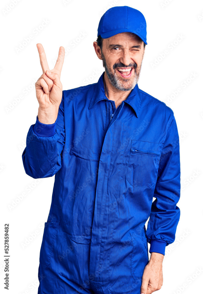 Middle age handsome man wearing mechanic uniform smiling with happy face winking at the camera doing victory sign with fingers. number two.