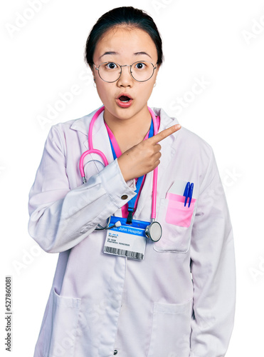 Young chinese woman wearing doctor uniform and stethoscope surprised pointing with finger to the side  open mouth amazed expression.