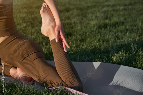A young woman practices yoga while lying on a mat in the park.