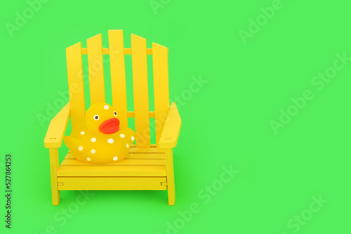 Photography Time for a rest composition with modern yellow wooden chair and spotted squeaky toy duckling on vivid green background