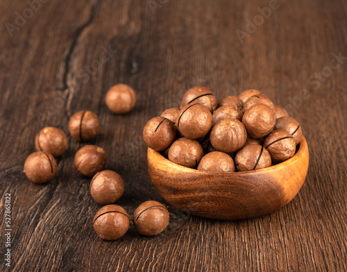 Macadamia nuts in a bowl and on a wooden background.