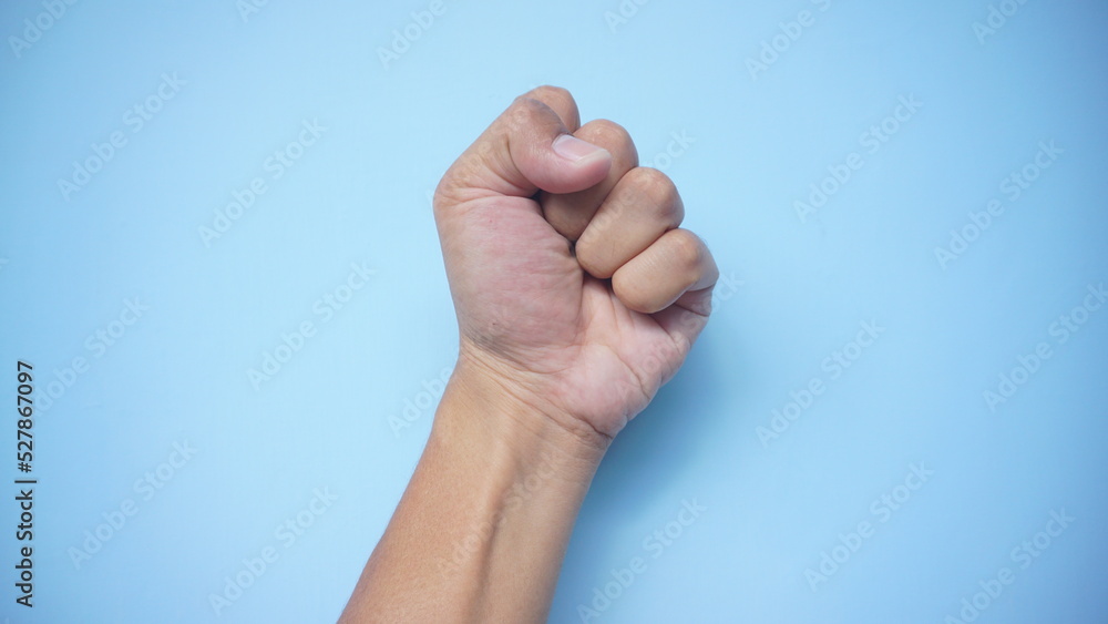 Male fist isolated on blue background. Asian clenched hand, gesturing up. Counting, aggression, brave, masculinity concept Male fist isolated on blue background. Asian clenched hand, gesturing up. Counting, aggression, brave, masculinity concept