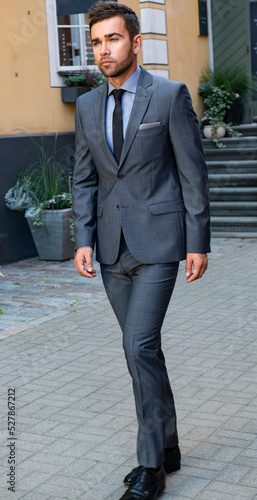 A man in a gray business suit walks around the city and poses
