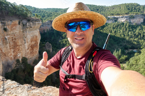 Fotografie a man in a hat and sunglasses takes a selfie with a nod of approval from a cliff