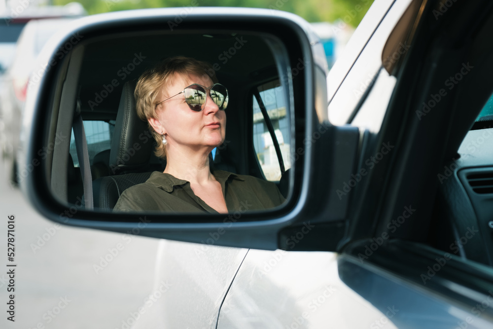 Reflection of a middle-aged woman driving a car in the car's side mirror. Woman driving a car. Portrait of a serious woman.