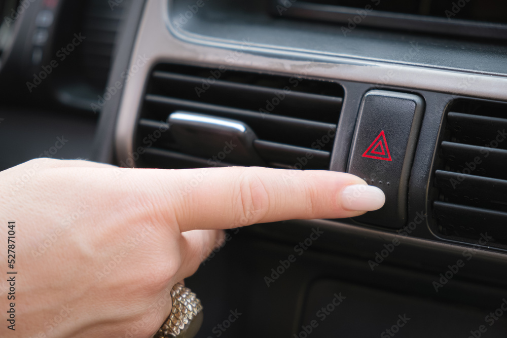 Driver presses his finger on the button to turn on the emergency stop signal. Woman clicks on emergency stop button. Activation of alarm signal. Close-up of a hand.