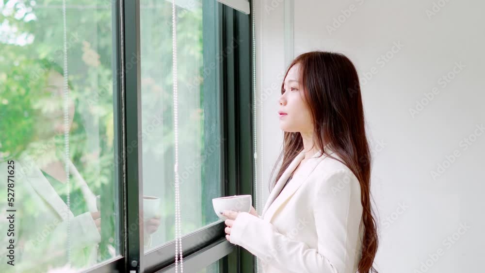 Asian business women wear suits are stand front windows in the office with drinking coffee in morning to relax, work on analytics, planning, marketing finance, profit company, entrepreneur, startup. Asian business women wear suits are stand front windows in the office with drinking coffee in morning to relax, work on analytics, planning, marketing finance, profit company, entrepreneur, startup.
