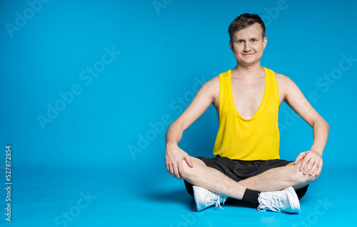 lean sportsman in a yellow t-shirt and black shorts on a blue background. sitting cross-legged on the floor