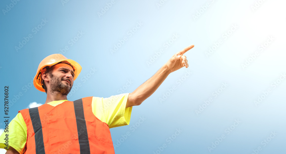 A portrait of a worker stands with confidence in an orange work suit and safety helmet against the sky. Smart industrial worker work concept. A portrait of a worker stands with confidence in an orange work suit and safety helmet against the sky. Smart industrial worker work concept.