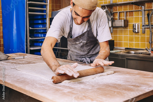 Crop male cook rolling dough in bakery photo