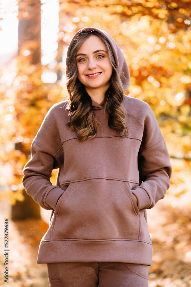 Young woman in hoodie sweater in autumn park. Sunny weather. Fall season. Young woman in hoodie sweater in autumn park. Sunny weather. Fall season.