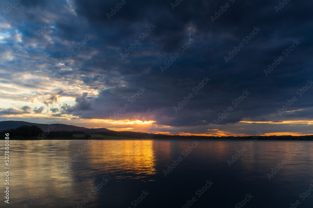 Majestic sunset dramatic sky above pond and distant hil. Czech landscape, long exposure