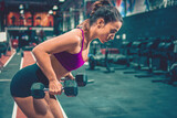 Young sportswoman in deadlift position exercising with dumbbells in the gym.