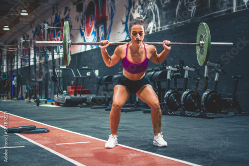 Strong sportswoman in squat position lifting heavy weights over her shoulders in the gym photo