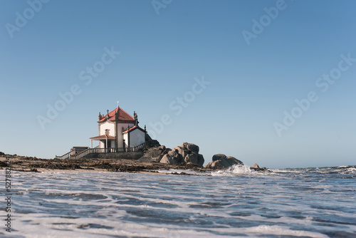 Old chantry facade against foamy ocean under blue sky