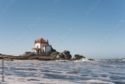 Old chantry facade against foamy ocean under blue sky photo