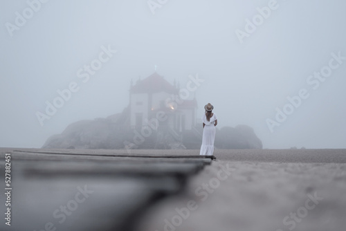 Anonymous traveler contemplating chantry and sea in mist from dock photo
