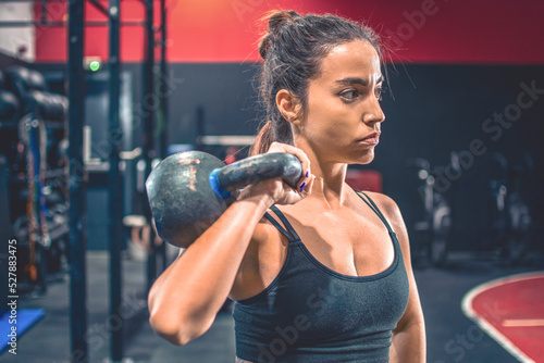 Portrait of beautiful young sporty woman with weight over shoulder in a gym