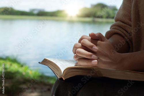 Foto A woman puts her hands on the bible for devotion and prays alone at the lake in the morning during the sun rises