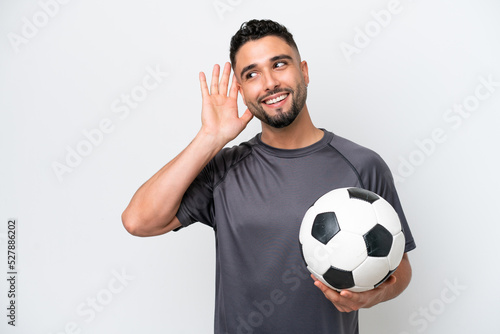 Arab young football player man isolated on white background listening to something by putting hand on the ear
