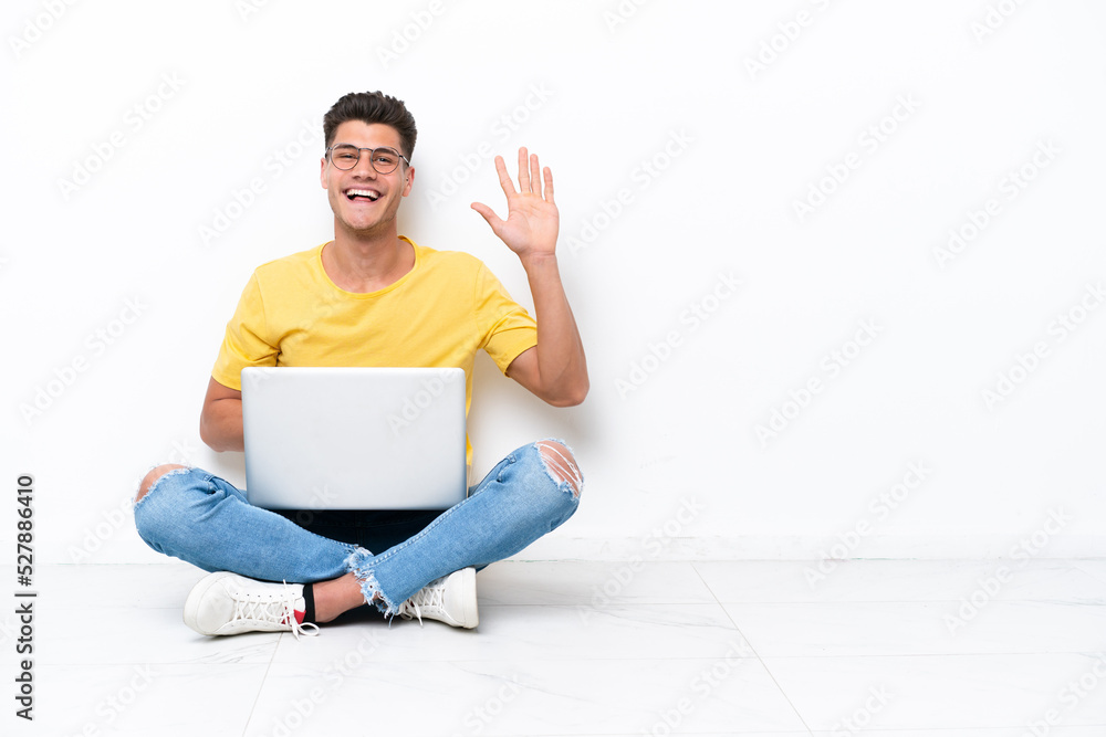 Young man sitting on the floor isolated on white background saluting with hand with happy expression Young man sitting on the floor isolated on white background saluting with hand with happy expression