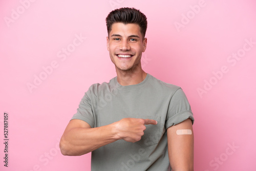 Young caucasian man wearing band-aids isolated on pink background and pointing it
