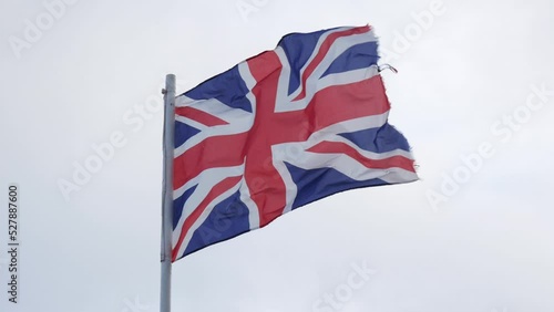 Lightly battered British flag waving in wind on gray sky background, Union Flag or Union Jack closeup