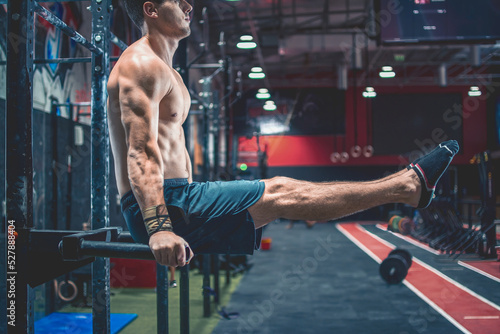 Fotografie Cropped photo of young handsome shirtless man's body in L Sit position on parallel bars during Calisthenic workout at gym