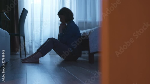 Lonely and sad woman sits in a dark room. The concept of a person in a state of depression or stress. Violence in family. photo