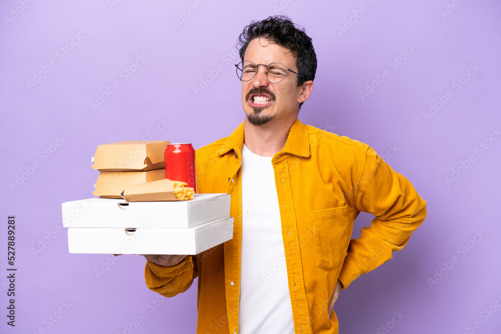 Young caucasian man holding fast food isolated on purple background suffering from backache for having made an effort Young caucasian man holding fast food isolated on purple background suffering from backache for having made an effort