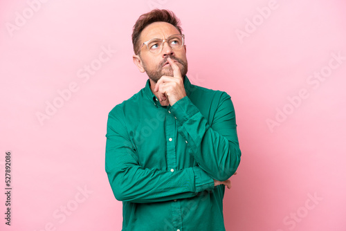 Middle age caucasian man isolated on pink background having doubts while looking up © luismolinero