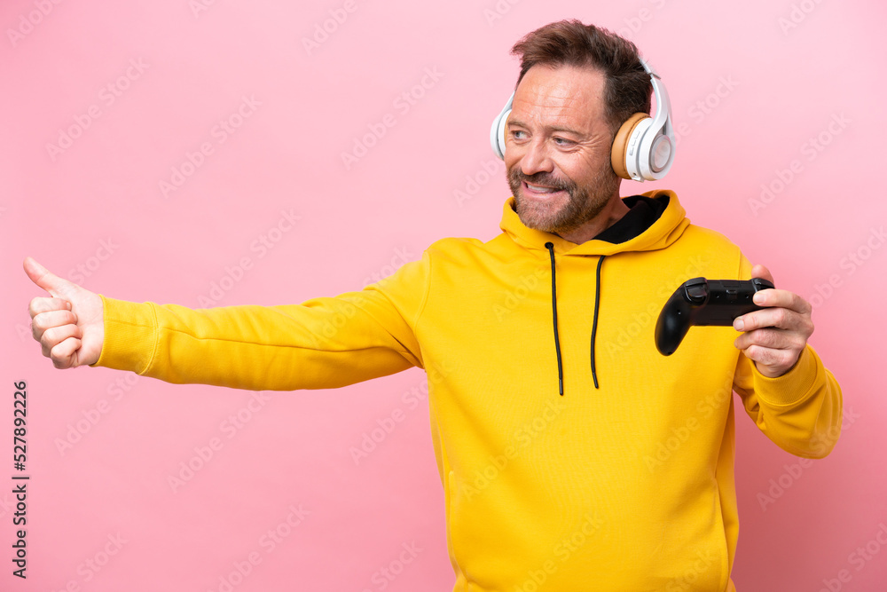Middle age man playing with a video game controller isolated on pink background giving a thumbs up gesture Middle age man playing with a video game controller isolated on pink background giving a thumbs up gesture