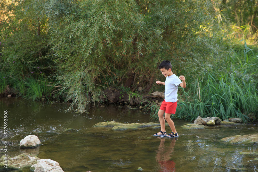 child crosses a river with a low riverbed in summer. Adventure games child crosses a river with a low riverbed in summer. Adventure games