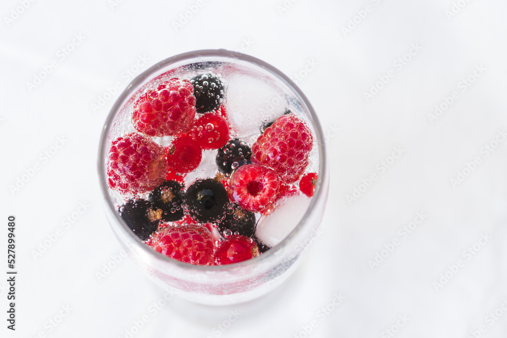 Carbonated drinks with fresh berries and ice. Fresh cold sparkling bubble water with raspberry, black and red currant berries in transparent glass with ice, top view macro. Food and drink concept Carbonated drinks with fresh berries and ice. Fresh cold sparkling bubble water with raspberry, black and red currant berries in transparent glass with ice, top view macro. Food and drink concept