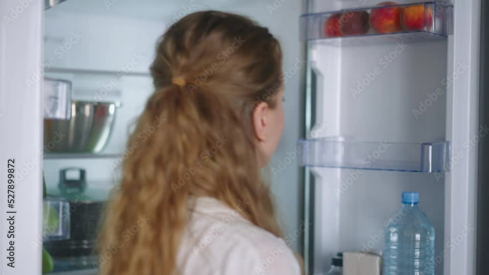 Woman putting groceries in new modern fridge. Young adult female unpacking shopping bag loading modern hi-tech refrigerator. Girl putting fruit and vegetables into fridge closeup shot Woman putting groceries in new modern fridge. Young adult female unpacking shopping bag loading modern hi-tech refrigerator. Girl putting fruit and vegetables into fridge closeup shot