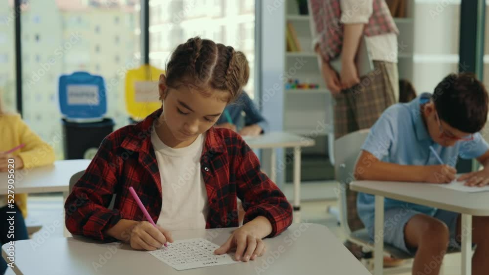 Caucasian brunette school girl is doing test thinking about answers in the classroom. Elementary school. Learning and education concept. Caucasian brunette school girl is doing test thinking about answers in the classroom. Elementary school. Learning and education concept.