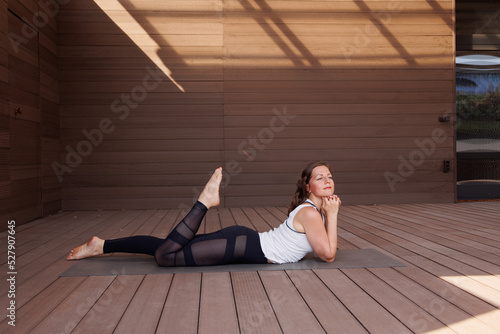 Beautiful strong muscular woman doing stretching on mat on terrace outdoors. Healthy young adult girl in sportswear stretch alone. Fit thin gimnast doing yoga, training on mat 