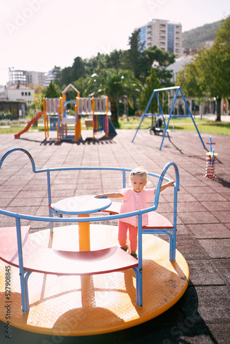 Little girl sits on a carousel seat in the playground. High quality photo